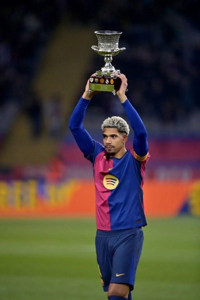 Barcelona's Uruguayan defender #04 Ronald Federico Araujo da Silva holds Barcelona's Spanish Super Cup trophy prior the Spanish Copa del Rey (King's Cup) last 16 first leg football match between FC Barcelona and Real Betis at the Estadi Olimpic Lluis Companys in Barcelona on January 15, 2025.  MANAURE QUINTERO / AFP