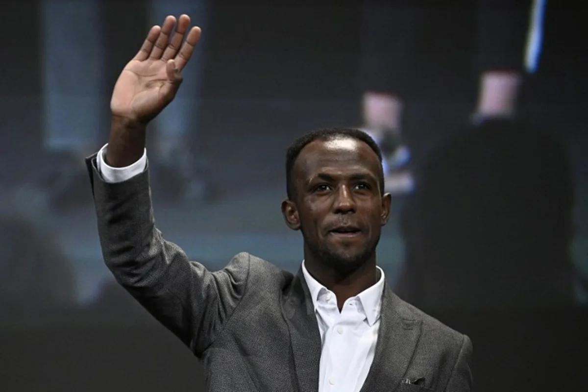 Eritrean cyclist Biniam Girmay waves as he arrives on stage for the 2025 Tour de France and the 2025 Tour de France Femmes (women) routes' presentation in Paris on October 29, 2024. The Tour de France Men's race will start in Lille, northern France on July 5, 2025 (July 5 - 27) and the women's race (July 26 - August 3) will be launched in Brittany. JULIEN DE ROSA / AFP