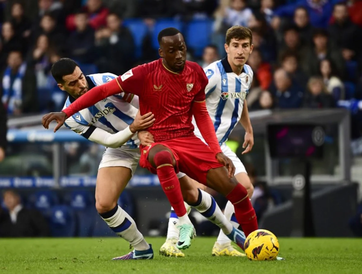 Real Sociedad's Spanish midfielder #8 Mikel Merino (L) vies with Sevilla's Belgian forward #11 Dodi Lukebakio (C) during the Spanish league football match between Real Sociedad and Sevilla FC at the Anoeta stadium in San Sebastian on November 26, 2023.   ANDER GILLENEA / AFP