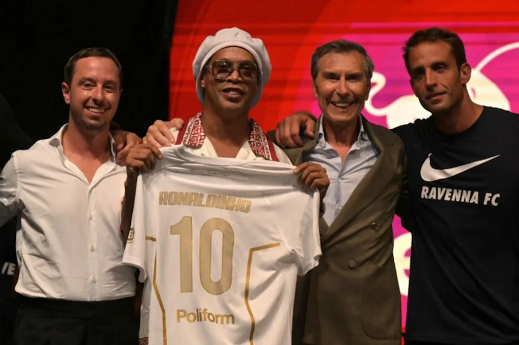 Newly recruited Brazilian football player Ronaldinho poses on stage with the jersey of Ravenna FC next to the president of the club, Ignazio Cipriani (R) during the team presentation in Marina di Ravenna on August 20, 2026. Former Ballon d'Or and World Cup winner Ronaldinho is set to come out of retirement aged 46 to play for Ravenna in the Italian third tier. Stefano RELLANDINI / AFP