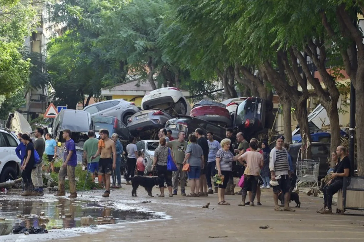 Residents gather in the street next to a pile of cars on October 31, 2024 after flash floods affected the town of Massanassa, in the region of Valencia, eastern Spain.  Rescuers raced on October 31, 2024 to find survivors and victims of once-in-a-generation floods in Spain that killed at least 95 people and left towns submerged in a muddy deluge with overturned cars scattered in the streets. About 1,000 troops joined police and firefighters in the grim search for bodies in the Valencia region as Spain started three days of mourning. Up to a year's rain fell in a few hours on the eastern city of Valencia and surrounding region on October 29 sending torrents of water and mud through towns and cities. JOSE JORDAN / AFP