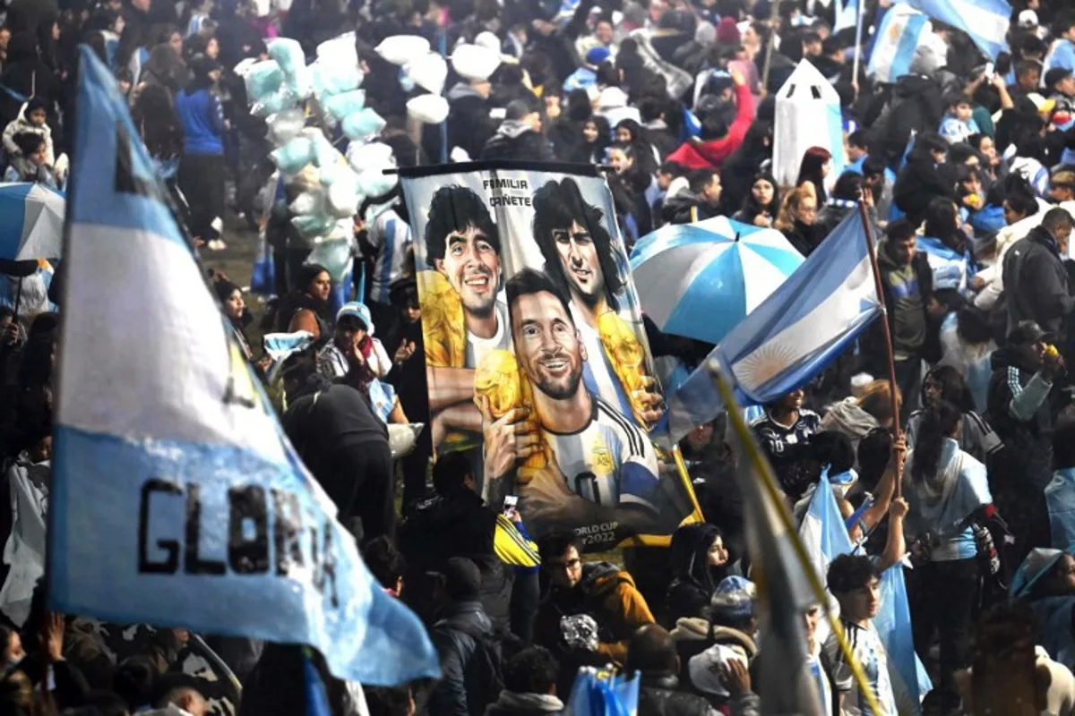 Fans hold a banner depicting Argentine football legends Diego Maradona, Mario Kempes and Lionel Messi holding FIFA World Cup trophies as supporters gather near the Argentine Football Association (AFA) training camp in Ezeiza, Buenos Aires Province, on July 20, 2026, while awaiting the arrival of Argentina's national football team from the United States following its defeat in the 2026 FIFA World Cup final. Luis ROBAYO / AFP