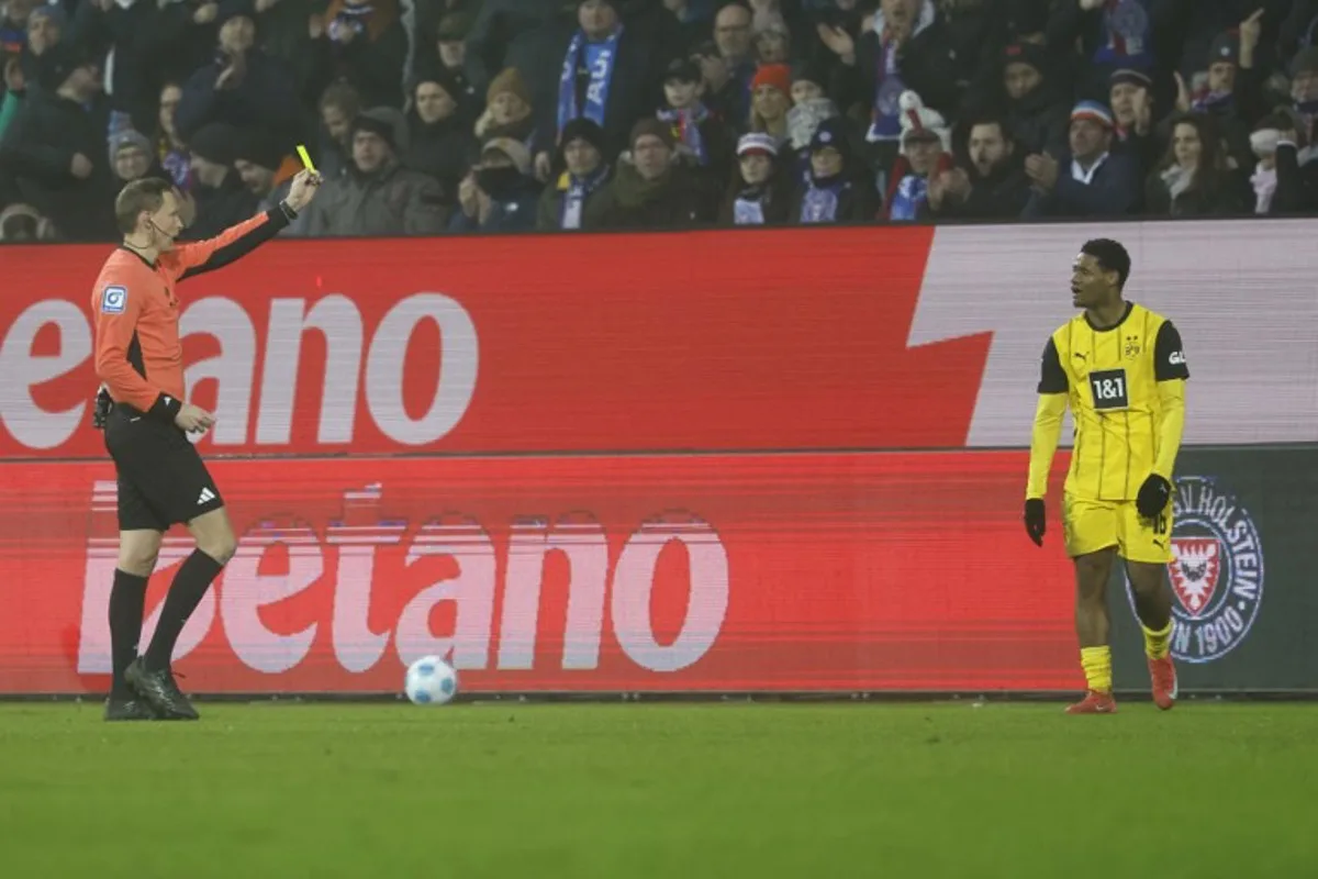 Dortmund's Belgian forward #16 Julien Duranville (R) is shown a yellow card by the referee during the German first division Bundesliga football match between Holstein Kiel and Borussia Dortmund in Kiel, northern Germany, on January 14, 2025.  Axel Heimken / AFP