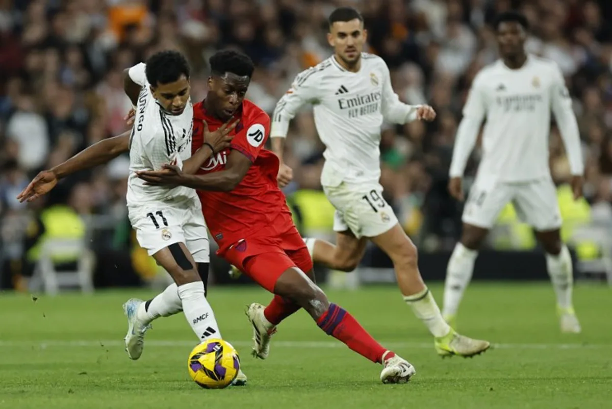 Real Madrid's Brazilian forward #11 Rodrygo and Sevilla's Belgian midfielder #12 Albert-Mboyo Sambi Lokonga (R) vie for the ball during the Spanish league football match between Real Madrid CF and Sevilla FC at the Santiago Bernabeu stadium in Madrid on December 22, 2024.  OSCAR DEL POZO / AFP