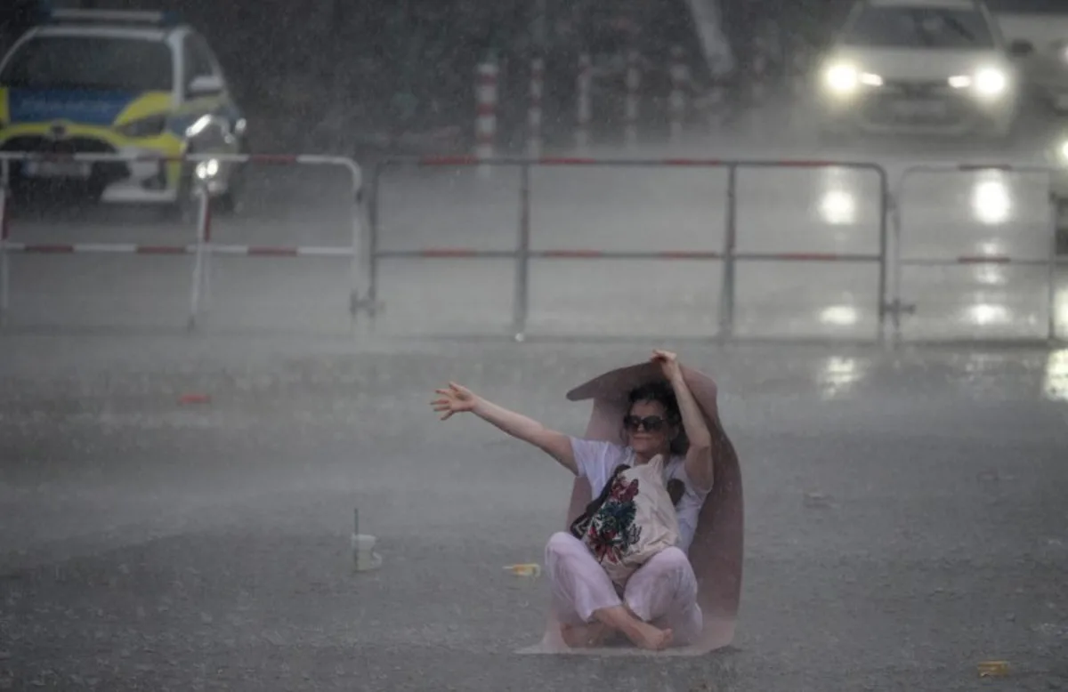 A woman uses a yoga mat to take shelter from the pouring rain as she takes part in the international yoga day, on June 21, 2026 in Berlin, Germany. RALF HIRSCHBERGER / AFP