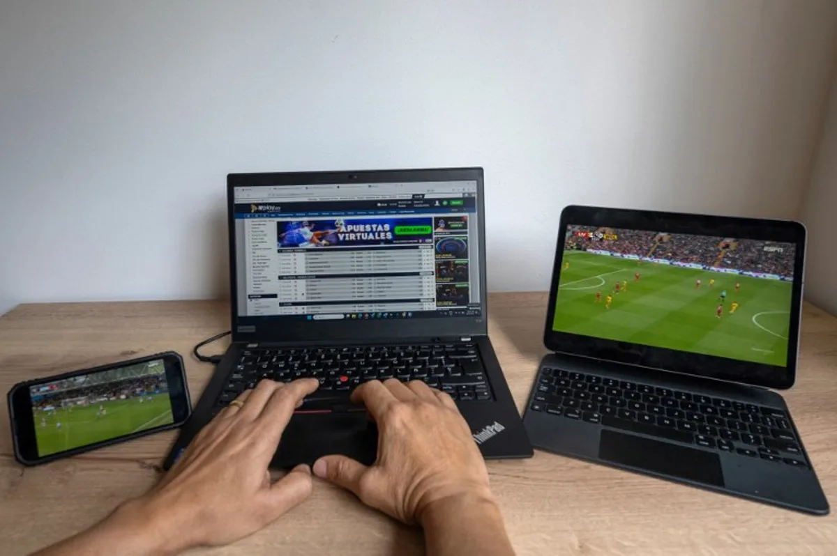 In this photo illustration taken on February 20, 2025, a user checks the betting company Wplay on a laptop while watching a football match in Bogota on February 17, 2025. For the first time, online sports betting will pay sales tax in Colombia. The worst armed conflict crisis in decades prompted the government to tax this important sector of the economy in a decision that strikes a chord with football fans. Luis ACOSTA / AFP