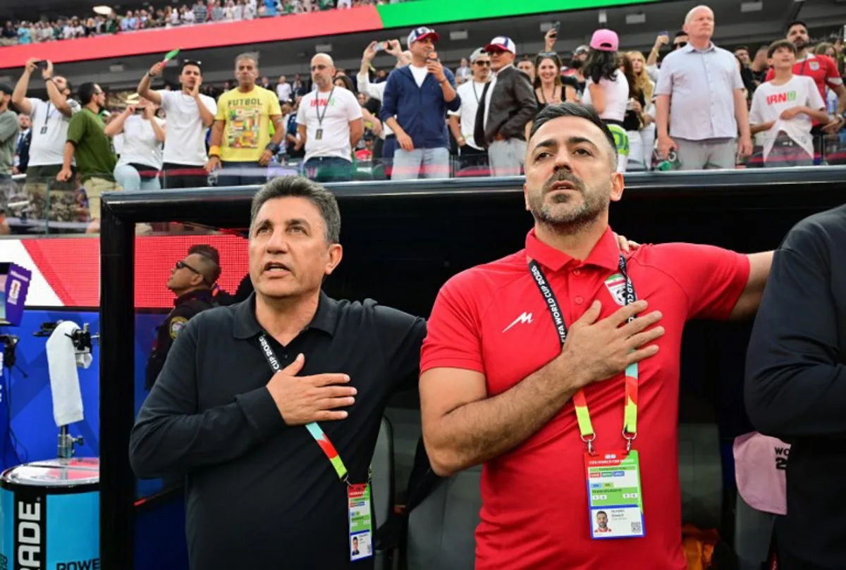 Iran's head coach Amir Ghalenoei (L) and assistant coach Saeed Alhoei (R) sing the national anthem ahead of the 2026 World Cup Group G football match between Iran and New Zealand at Los Angeles Stadium in Inglewood on June 15, 2026. Frederic J. Brown / AFP
