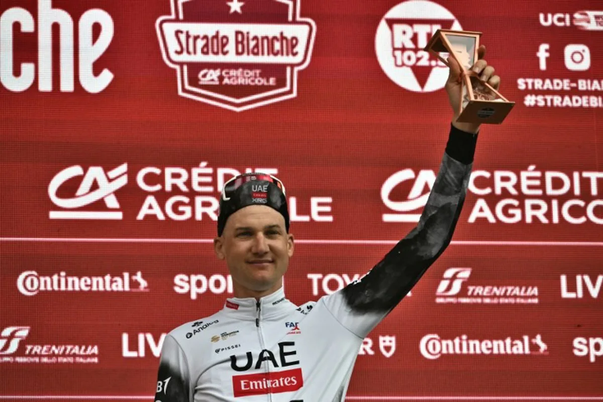 Third-placed Team UAE's Belgian rider Tim Wellens celebrates as he holds his trophy on the podium of the 19th one-day classic 'Strade Bianche' (White Roads) men's cycling race between Siena and Siena in Tuscany on March 8, 2025.   Marco BERTORELLO / AFP