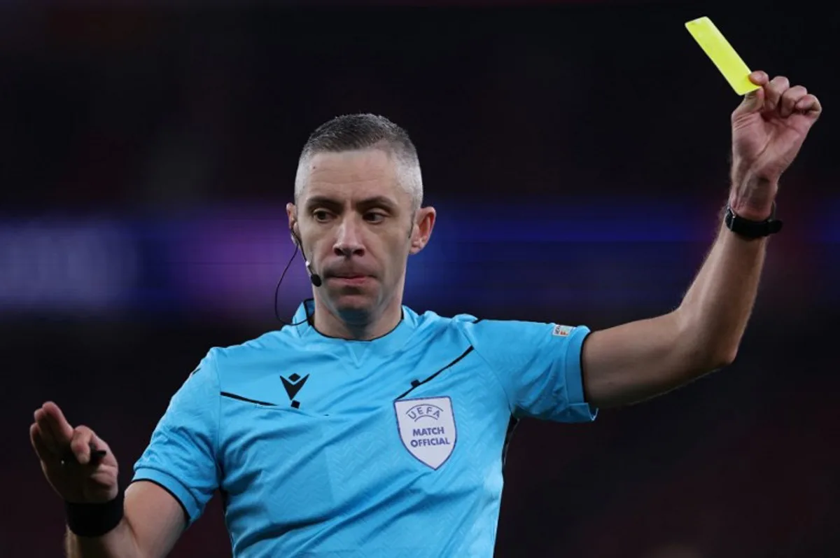 Romanian referee Radu Petrescu presents a yellow card during the UEFA Champions League, league phase football match between SL Benfica and Bologna FC 1909 at Estadio da Luz in Lisbon on December 11, 2024. FILIPE AMORIM / AFP