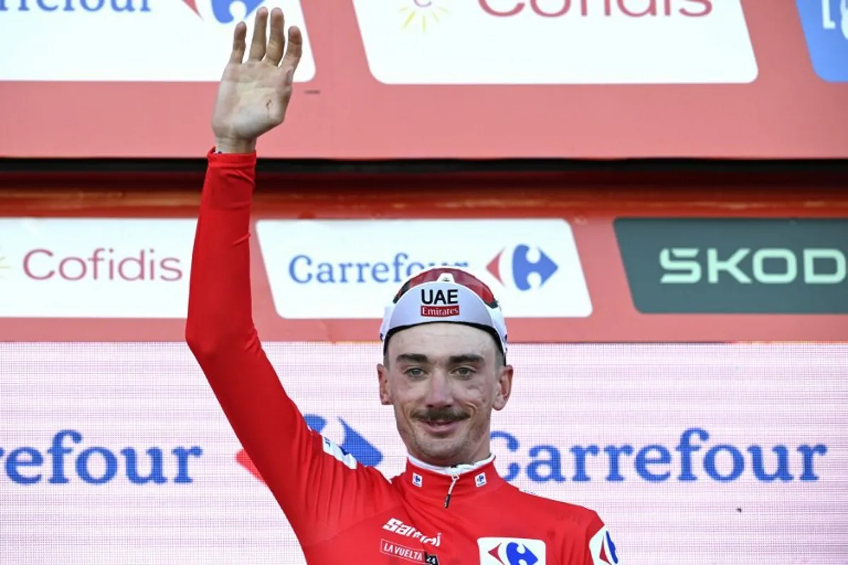 Team UAE's Brandon McNulty waves from the podium, wearing the red jersey of the general ranking leader after winning the stage 1 of La Vuelta a Espana cycling tour, a 12 km time-trial race from Lisbon to Oeiras, on August 17, 2024.   MIGUEL RIOPA / AFP