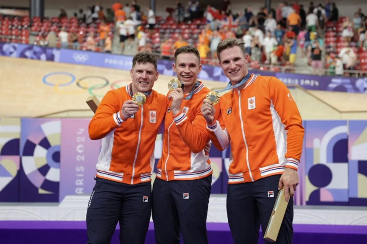 Netherlands' Roy van den Berg (L), Netherlands' Harrie Lavreysen (C) and Netherlands' Jeffrey Hoogland (R) celebrate their gold medal on the podium after winning the men's track cycling team sprint event of the Paris 2024 Olympic Games at the Saint-Quentin-en-Yvelines National Velodrome in Montigny-le-Bretonneux, south-west of Paris, on August 6, 2024.  Thomas SAMSON / AFP