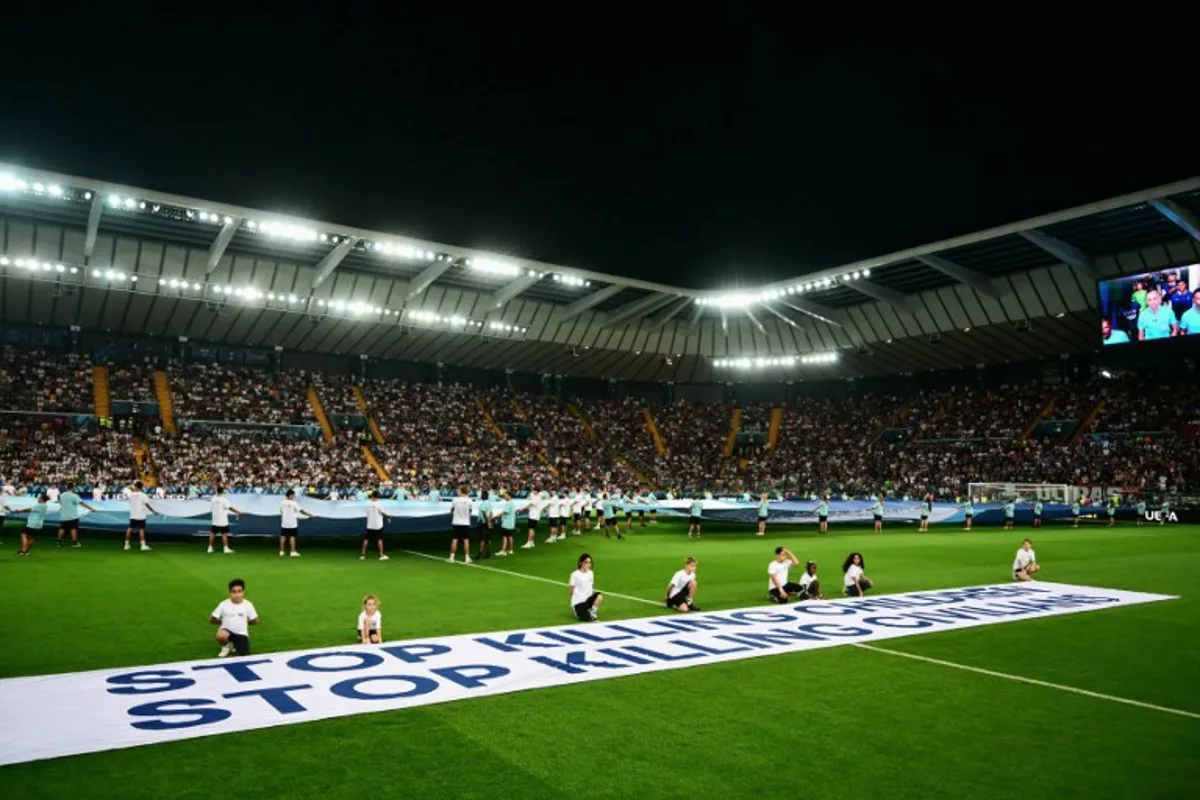 Mascots hold a banner which reads "Stop killing children, Stop killing civilians" on the pitch ahead of the 2025 UEFA Super Cup final football match between Paris Saint-Germain (FRA) and Tottenham Hotspur FC (ENG) at the Friuli stadium, in Udine, on August 13, 2025. Marco BERTORELLO / AFP