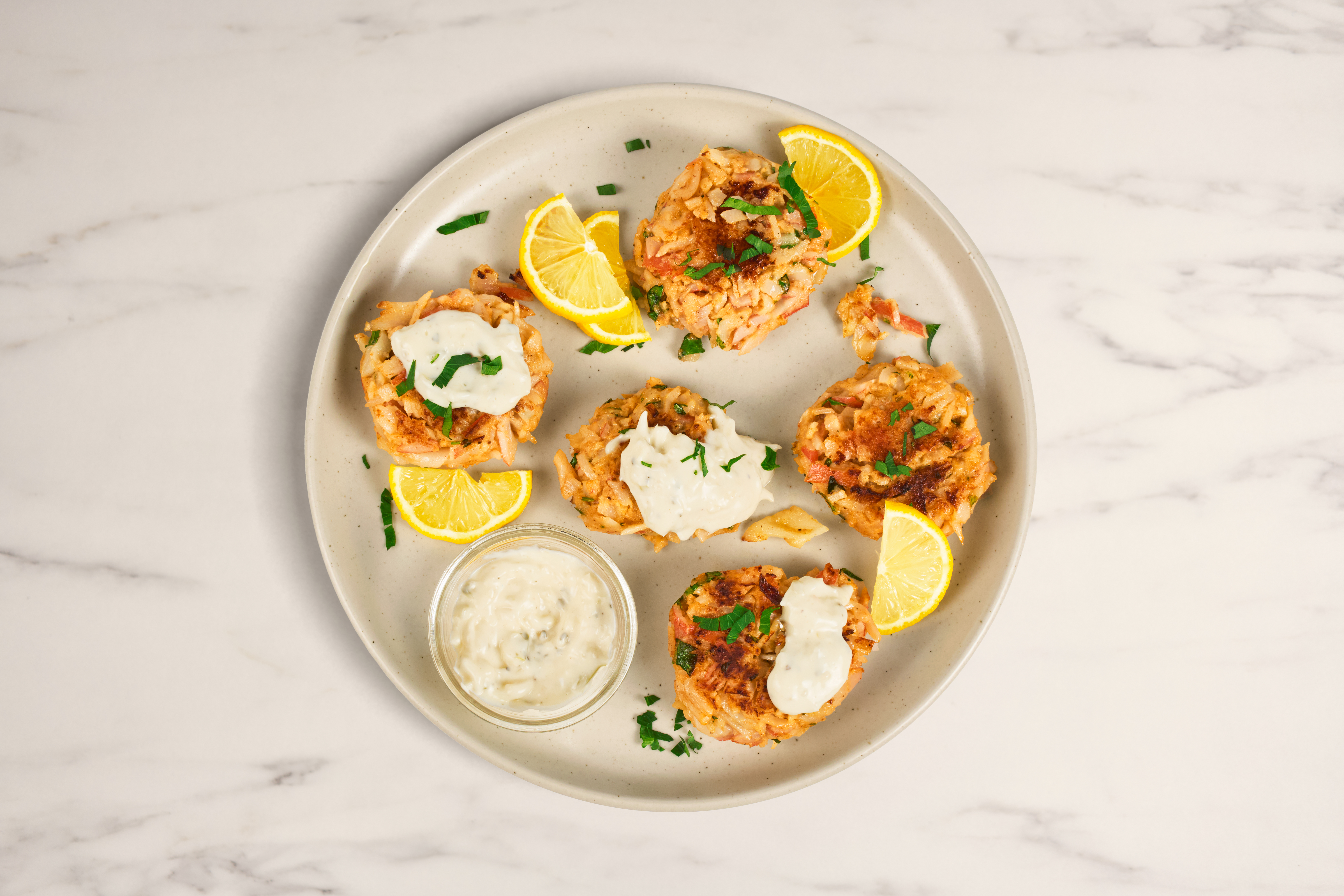 Crab cakes made in skillet with remoulade sauce on top and chive garnish.
