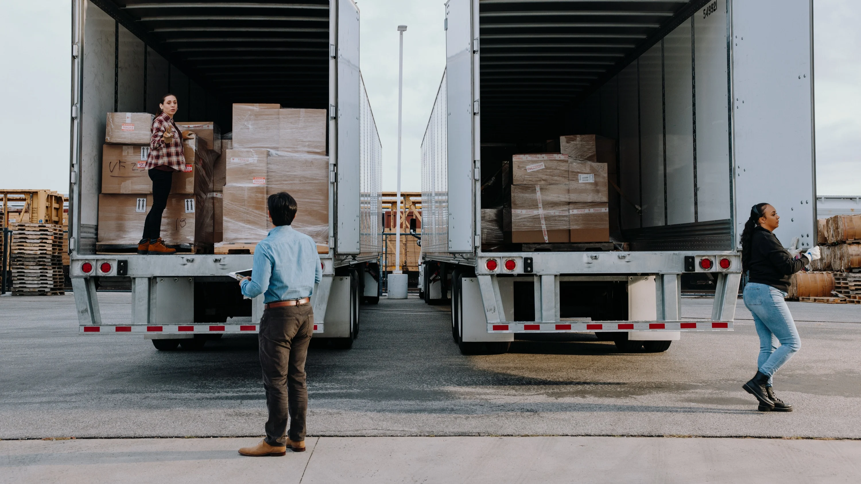 Two open shipping trucks loaded with boxed cargo, with a person standing in one truck and another on the ground.