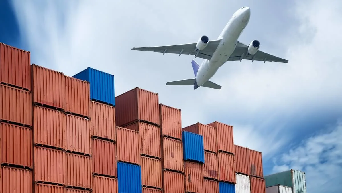 Row of stacked freight containers with an airplane flying over