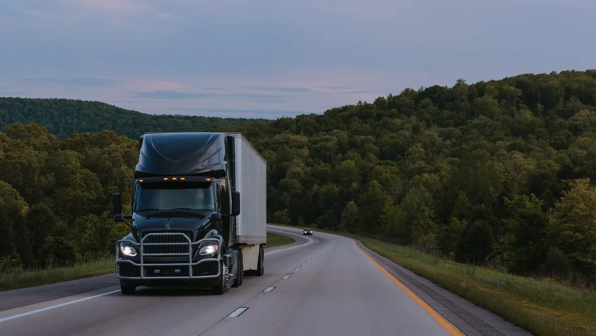 A black semi-truck drives along a scenic highway, representing dynamic carrier capacity across Uber Freight's network.