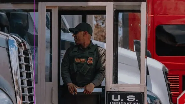 Border patrol officer in a U.S. Immigration and Customs booth between trucks at a border crossing checkpoint.