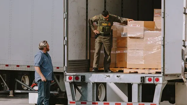 Delivery workers loading pallets of boxed merchandise onto a truck at a loading dock.