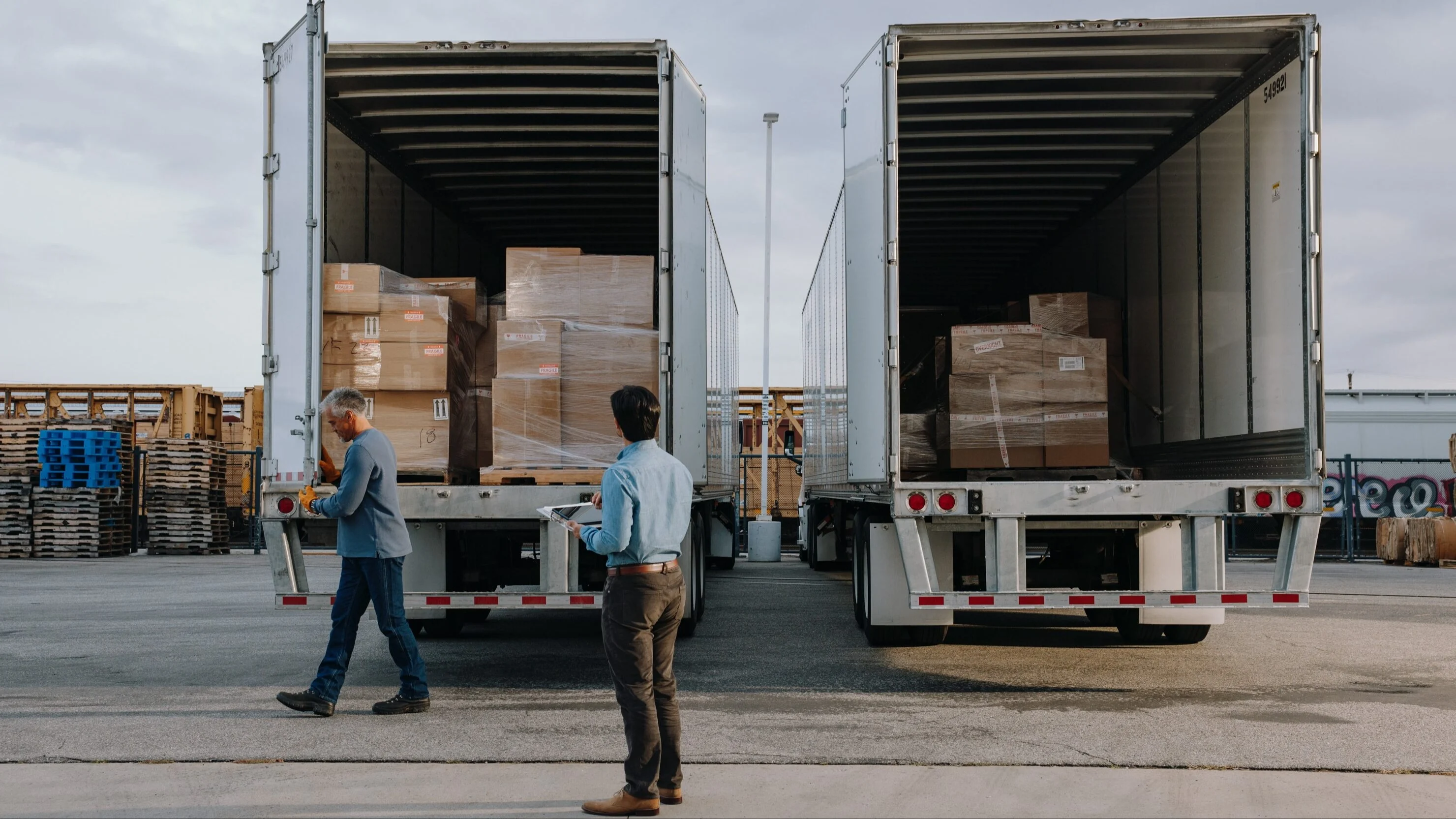 Two men standing behind trucks with open doors.