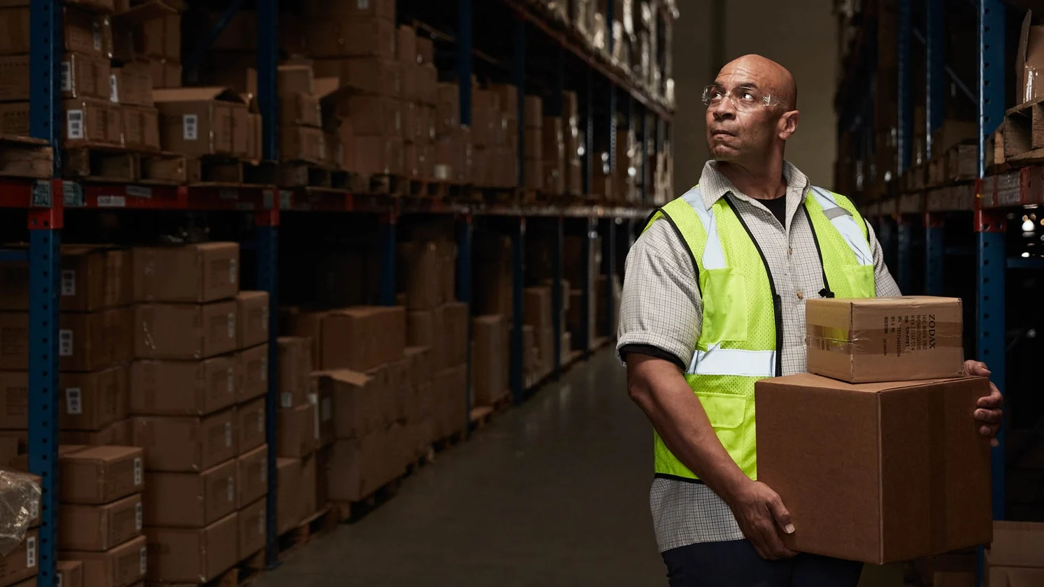 Man holding boxes looking up in warehouse.