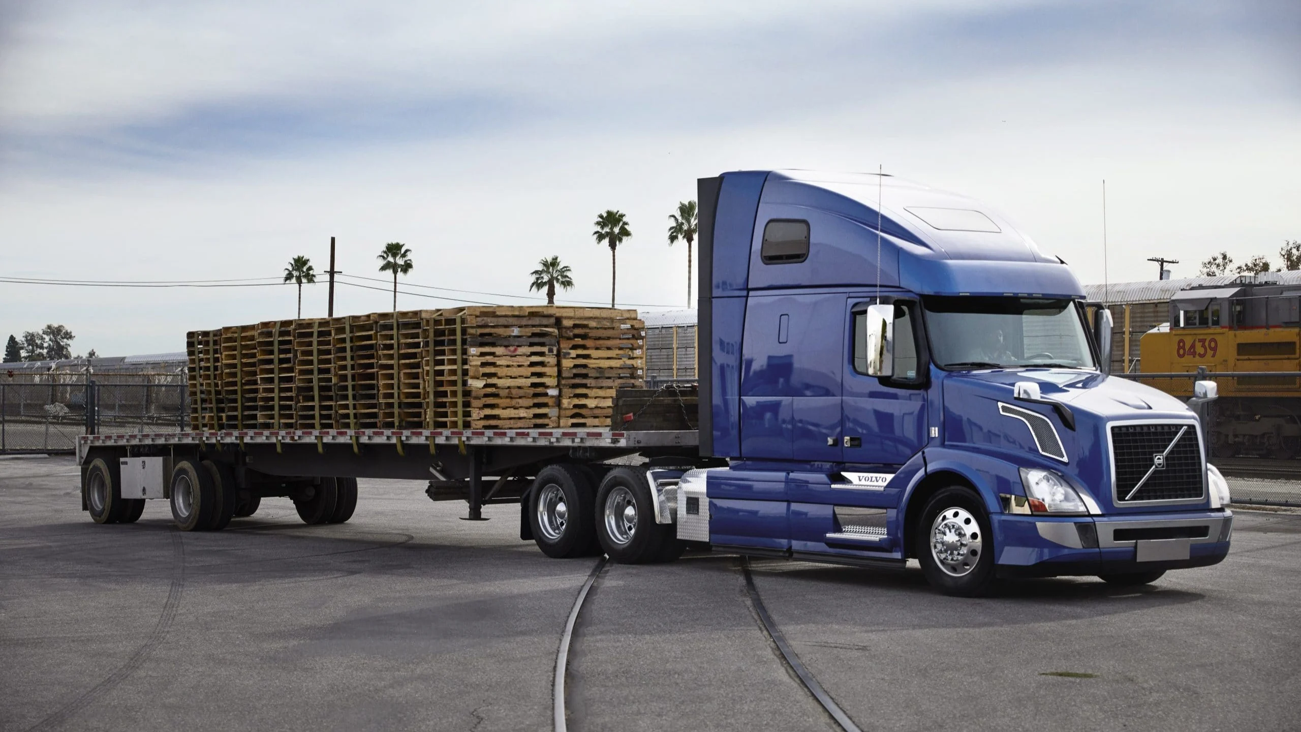 Blue truck with flatbed hauling pallets.