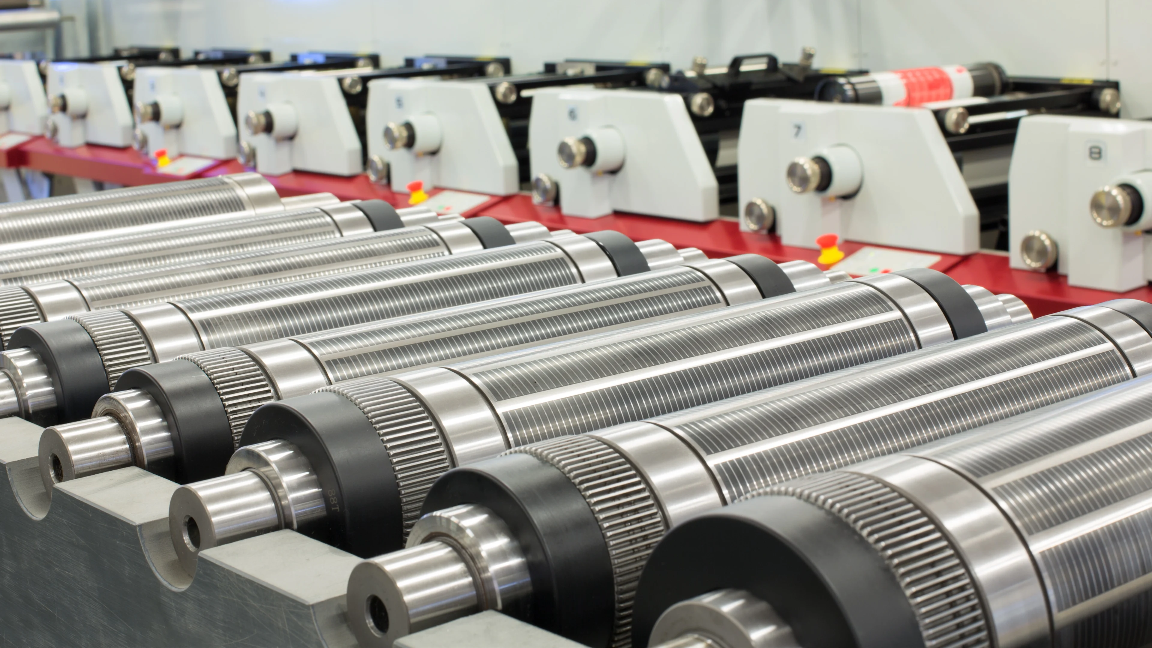 Rodillos industriales metálicos con superficies roscadas alineados en equipos de fabricación con componentes rojos visibles.