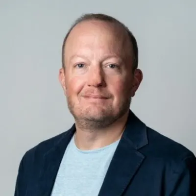 Headshot of Mike Doucleff, Head of Europe at Uber Freight, wearing a light blue shirt and dark blazer against a plain gray background.