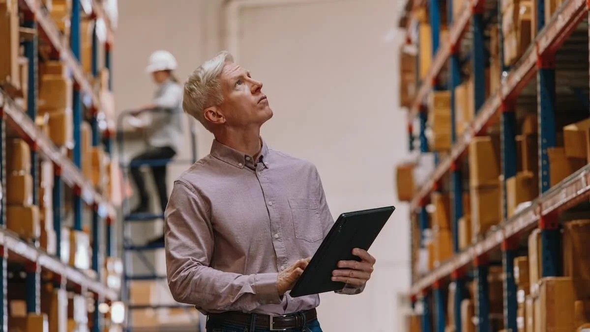 A grocer in a warehouse inspecting inventory holding a tablet