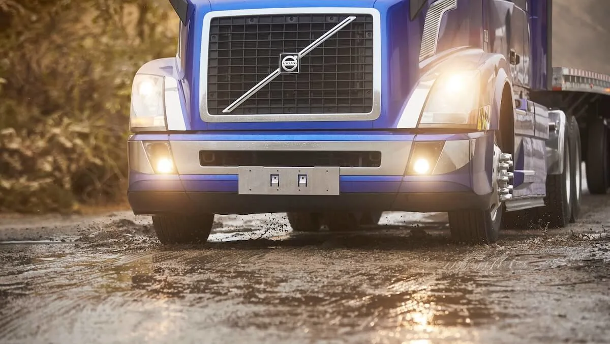 Front view of a blue truck with trailer driving on wet highway with it's lights on