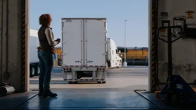 Person standing at loading dock entrance watching a white delivery truck in a shipping facility
