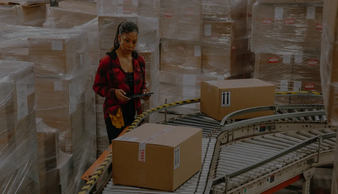 Woman viewing boxes on a conveyor belt.