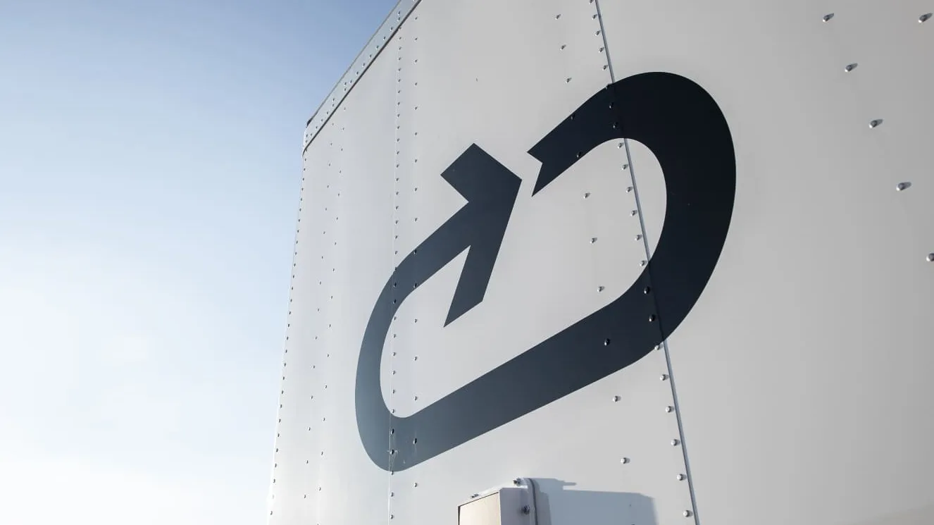 Black arrow logo on white metal surface of a delivery truck or shipping container against blue sky.