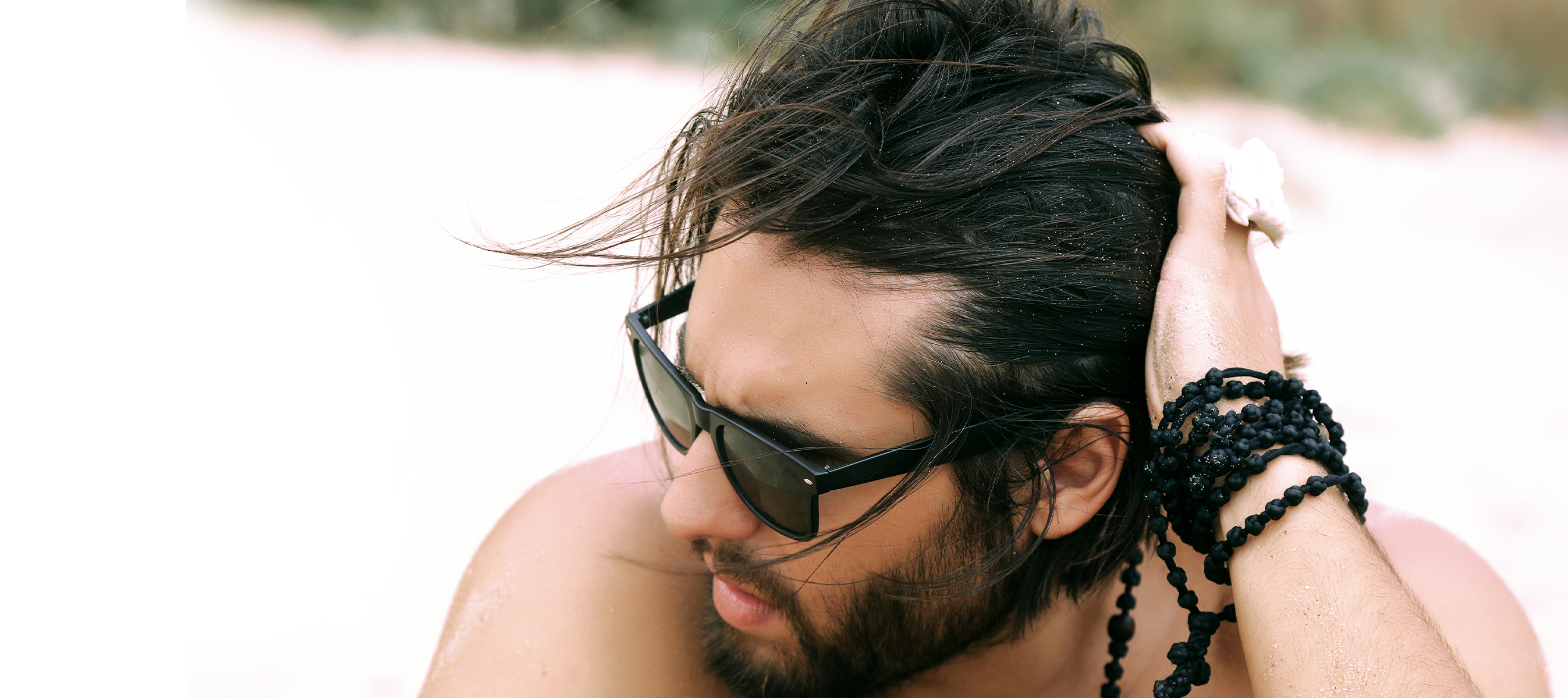 Portrait of hipster man with 1a straight hair in sunglasses and beard posing on the beach