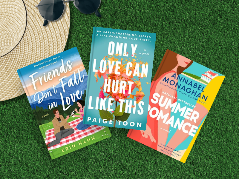 "Three summer lovin' novels on green grass with straw hat and sunglasses: Friends Don't Fall in Love by Erin Hahn (blue cover with picnic scene), Only Love Can Hurt Like This by Paige Toon (teal cover with romantic couple), and Summer Romance by Annabel Monaghan (colorful geometric cover design)."