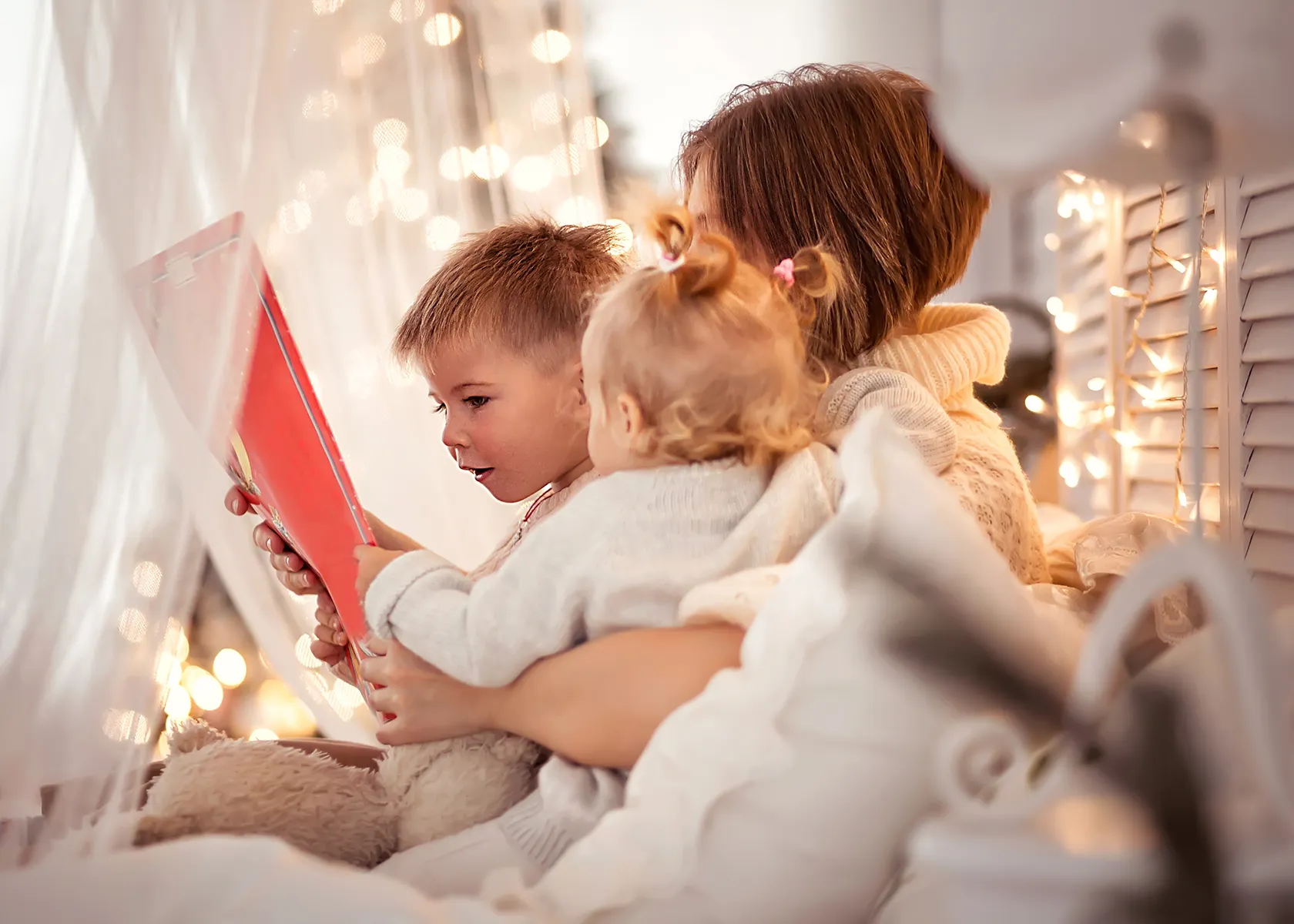 Bedtime reading moment with parent and child sharing red book in warm, softly lit bedroom promoting family literacy