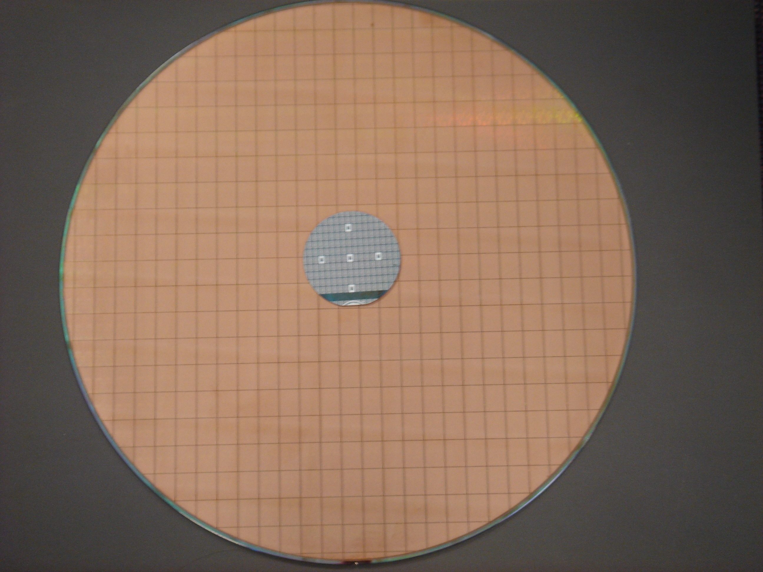 Produced on 2-inch wafers, the Intel 4004 processor — shown here in silver, resting on top of a modern 12-inch wafer — was one of the smallest microprocessor designs ever to go into commercial production.