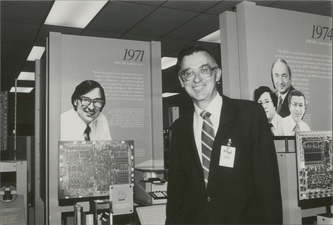 Marcian E. "Ted" Hoff Jr. posing with the Intel Museum exhibit about the invention of the 4004, feauring an image of his younger self.