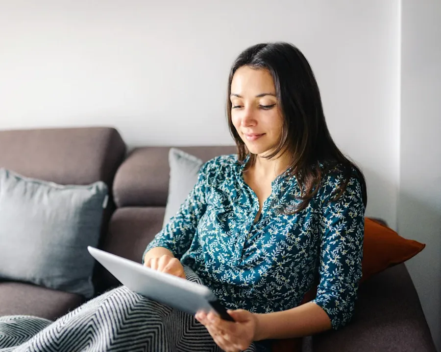 A person seated on a couch interacting with a tablet.