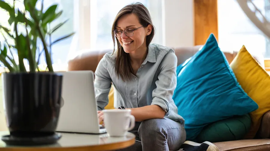 Female sitting on a couch with her laptop and a mug. 