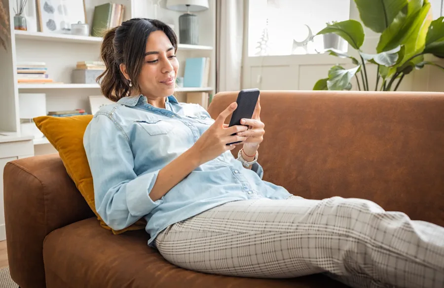 A person laying on a couch smiling, interacting with their phone.