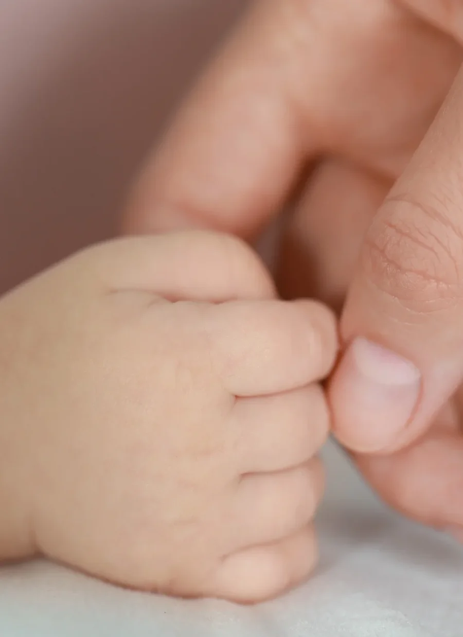 An adult hand embracing the hand of an infant. 