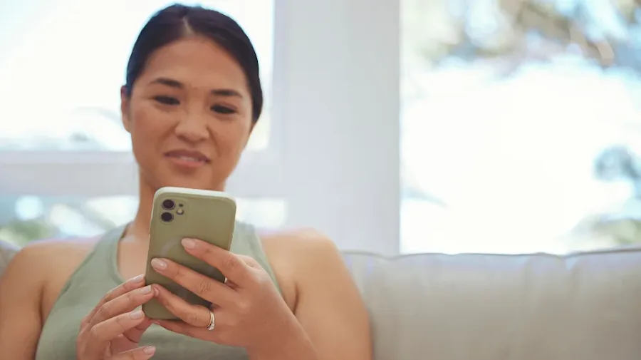 A smiling female holding her cell phone seated on a couch. 