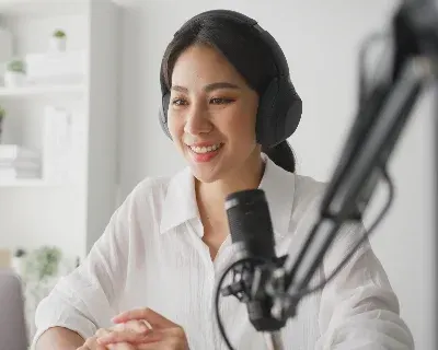 A person with headphone, smiling while speaking into a microphone.