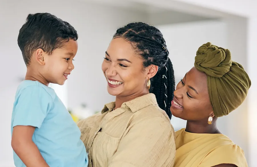 Two adults smiling, one holding a child smiling back.