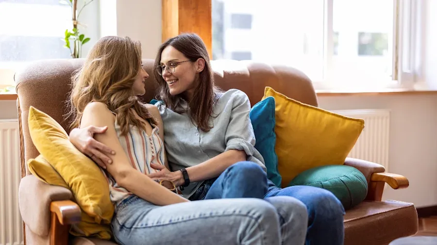 Two females on a couch, smiling and embracing.