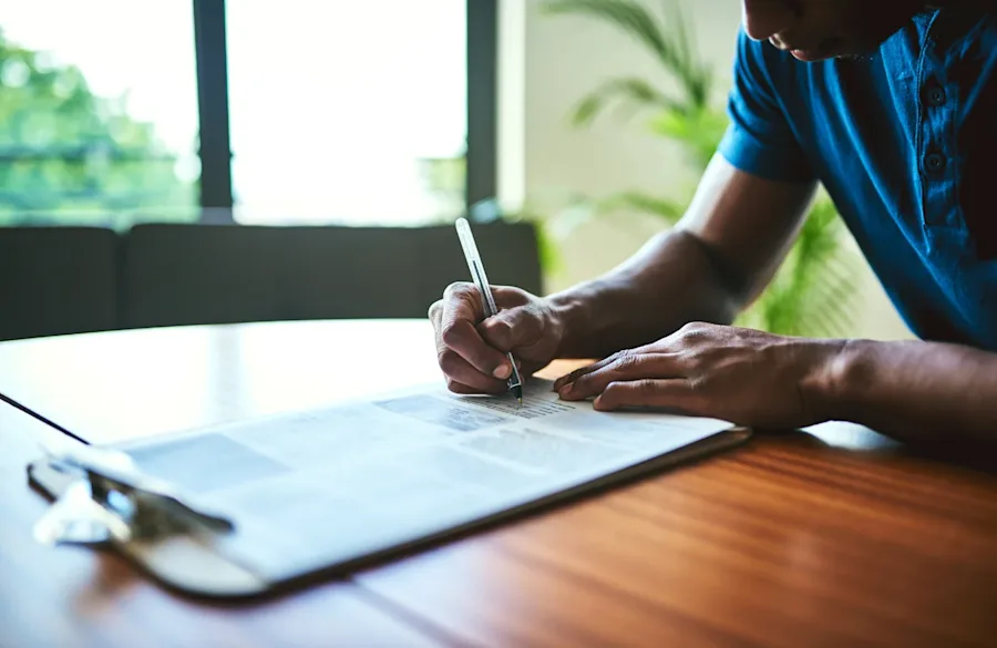 A person writing on paper attached to a clipboard.
