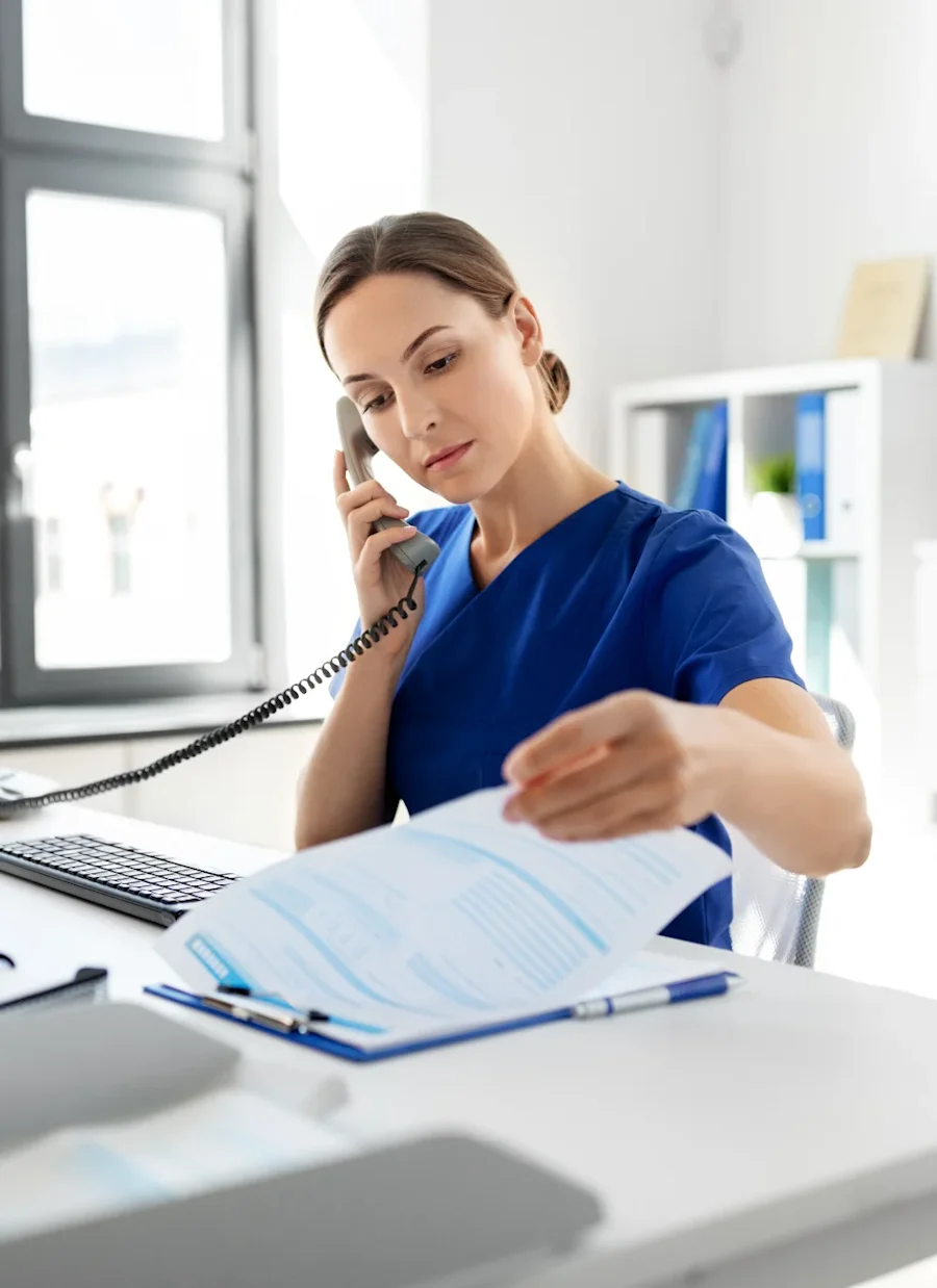 A physician reviewing information on a clipboard while on the phone.