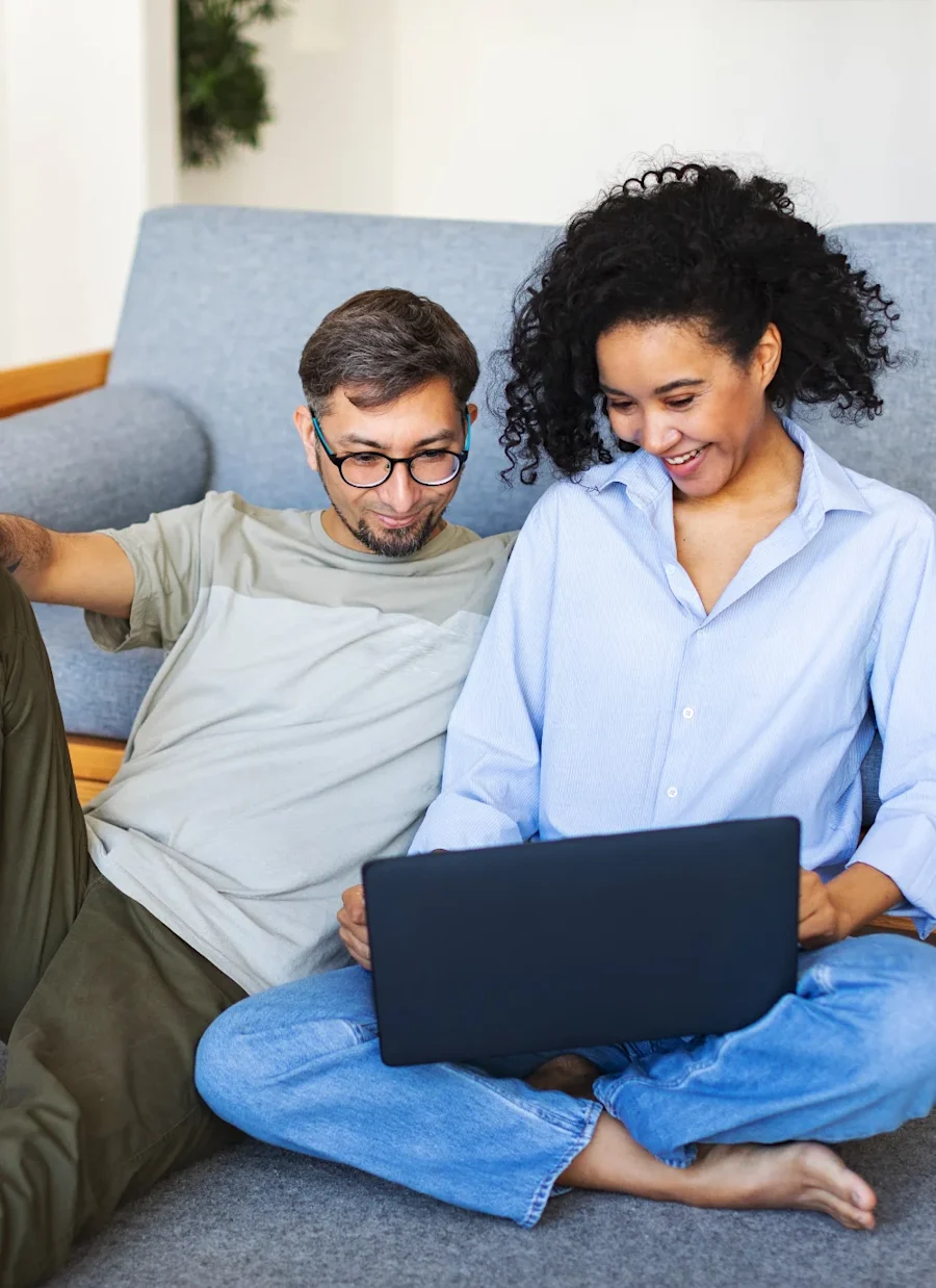 A couple seated together looking at a laptop smiling.