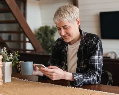 A person seated with a beverage, smiling at their phone.