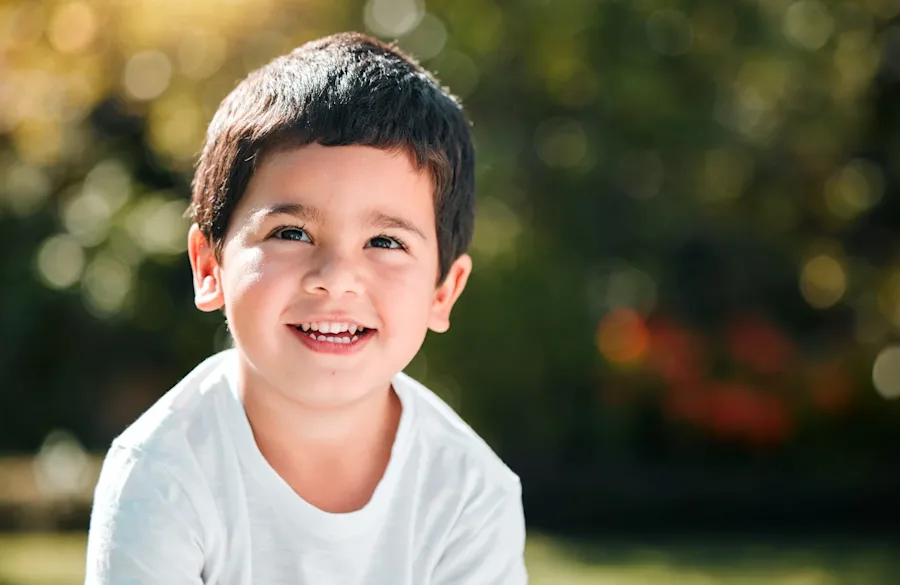 A young child smiling sitting outside.